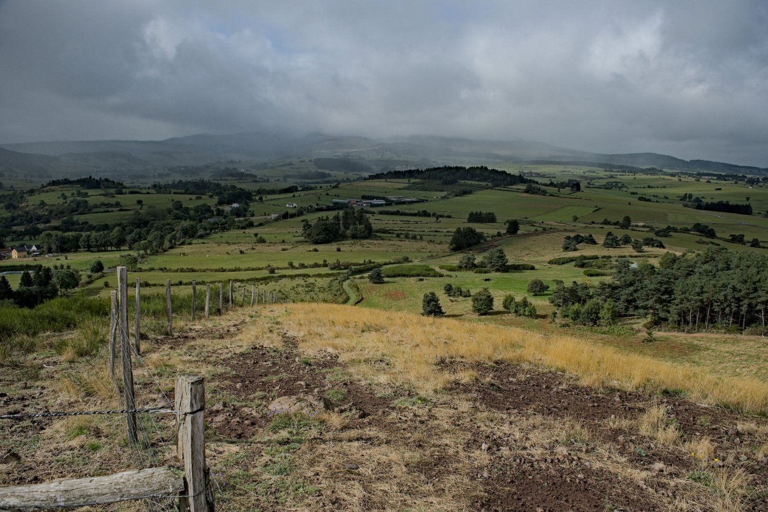 Paysage agricole depuis Combegrasse. Au fond sous les nuages les puys d'Augère (1243m) et de Combe-Perret (1380m)
